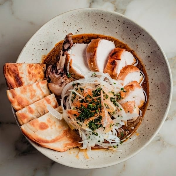 Overhead view of sliced chicken in a rich sauce, topped with onions and herbs, served with flatbread.