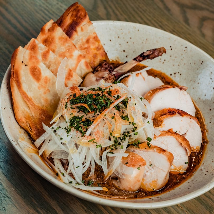 Sliced chicken breast and leg in sauce, topped with onions, herbs, and paprika, served with flatbread.