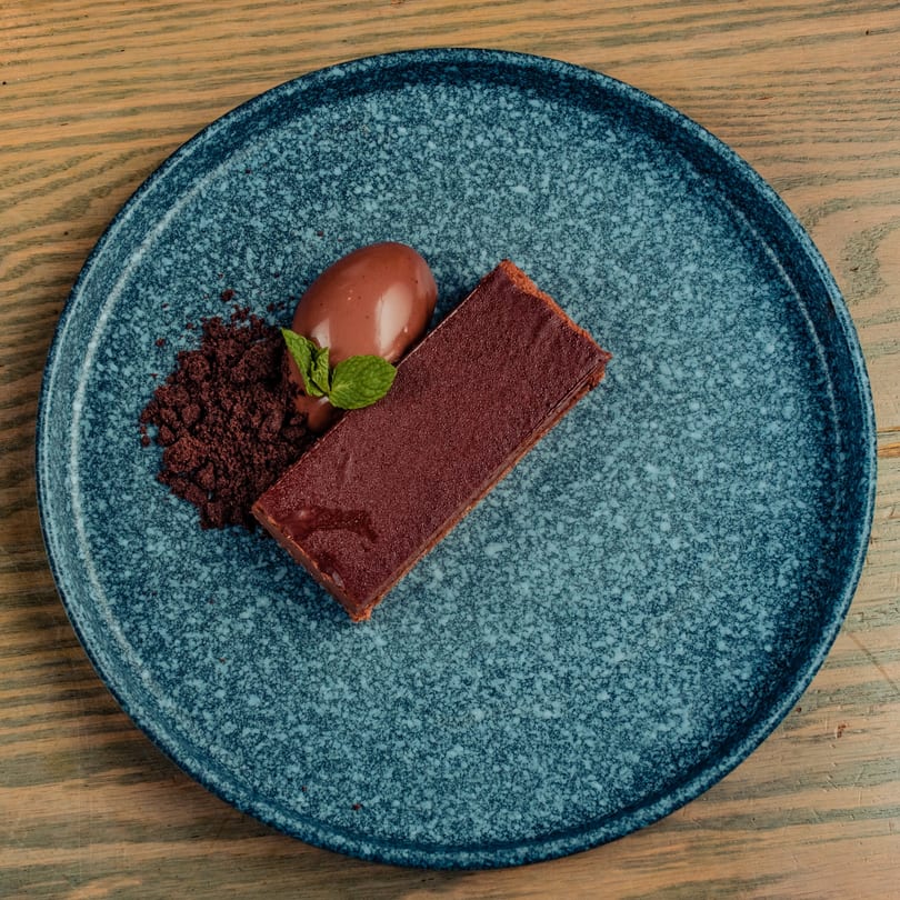 Chocolate dessert with a scoop of ice cream, chocolate crumbles, and a mint leaf on a blue plate.